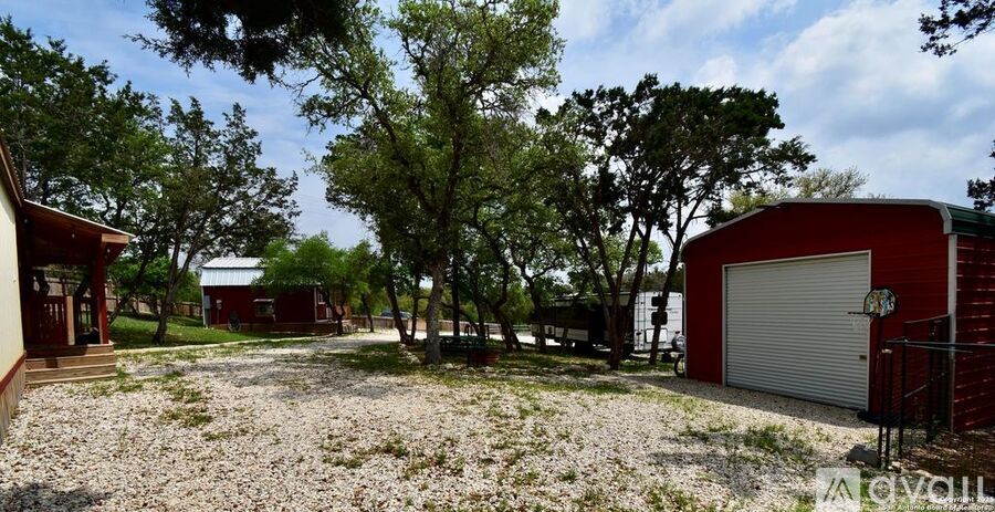 A red building with a white door is surrounded by trees and a gravel area.