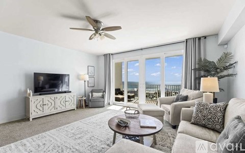 A living room with a television, a sofa, a coffee table, and a balcony with a view of the ocean.