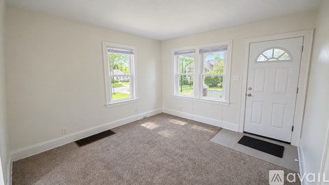 A room with a carpeted floor, a white door, and a window with a view of a green lawn.