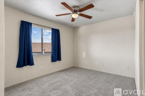 A room with a ceiling fan and a window with blue curtains.