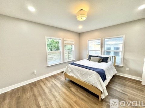 A bedroom with a bed, wooden floors, and windows.