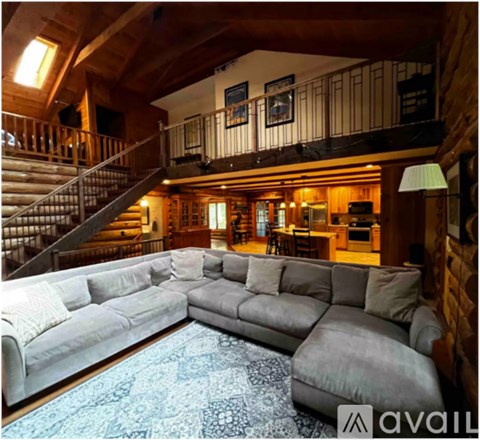 A large grey sectional sofa in a spacious room with wooden walls and a staircase.