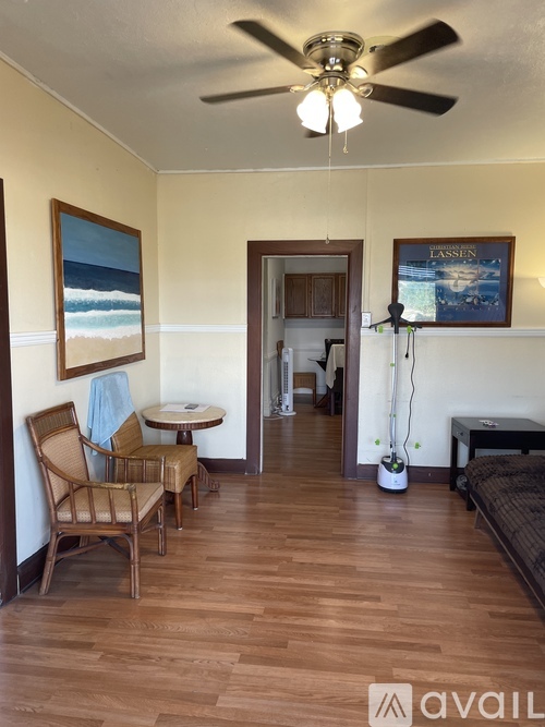 A room with a ceiling fan and a painting of a beach scene on the wall.