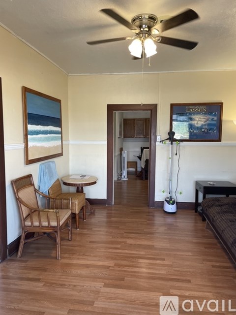 A room with a ceiling fan and a painting of a beach scene on the wall.