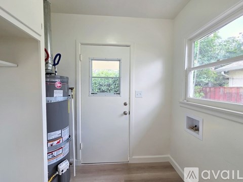 A white door is in a room with a window and a fridge.