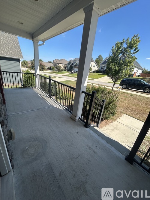 A balcony with a black railing and a view of a street with cars and houses.