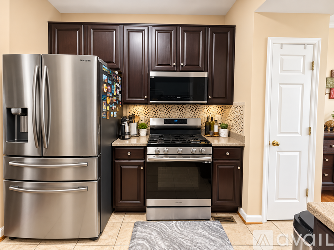 A kitchen with a stainless steel refrigerator and oven, brown cabinets, and a tile backsplash.