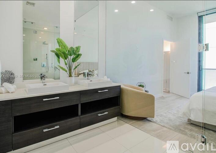 A modern bathroom with a large mirror, a sink, and a plant.
