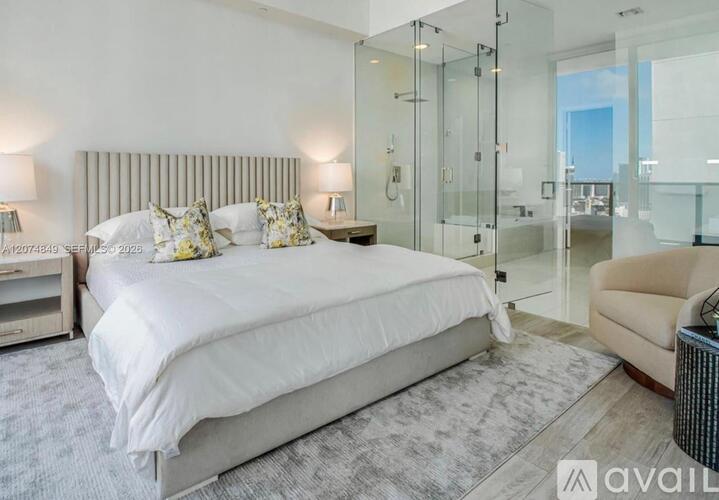 A bedroom with a large bed, a chair, and a glass shower.