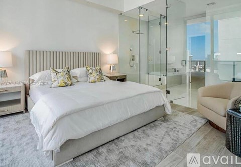 A bedroom with a large bed, a chair, and a glass shower.