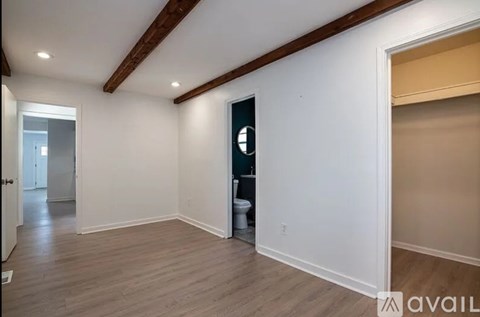 A spacious room with wooden floors and white walls, featuring a toilet in the corner.