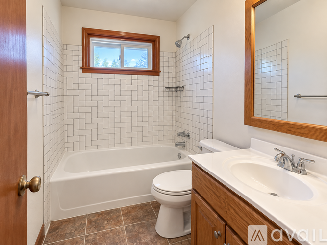 A white toilet sits in a bathroom with a white bathtub and a wooden medicine cabinet.