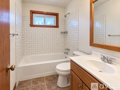 A white toilet sits in a bathroom with a white bathtub and a wooden medicine cabinet.