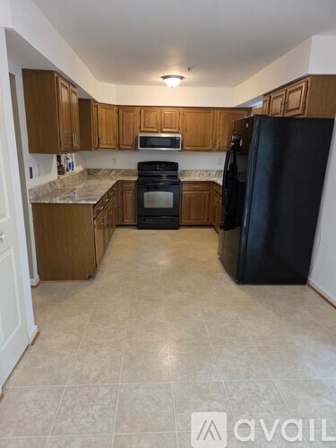 A kitchen with a black refrigerator and wooden cabinets.