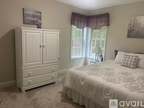 A bedroom with a bed, a dresser, and a window with a curtain.