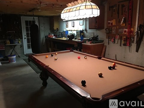 A pool table in a room with a workbench and tools in the background.