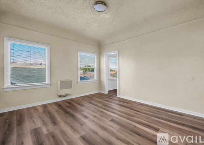 A room with wooden flooring and two windows, one of which has a view of a beach.