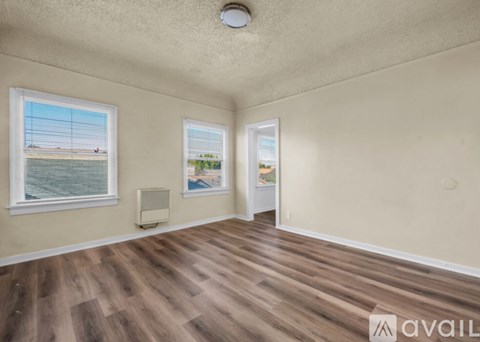 A room with wooden flooring and two windows, one of which has a view of a beach.