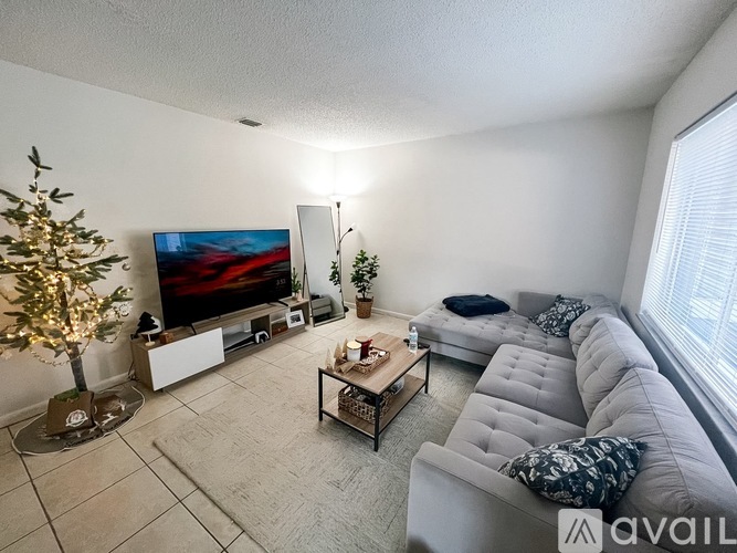 A living room with a grey couch, a coffee table, a television, and a Christmas tree.