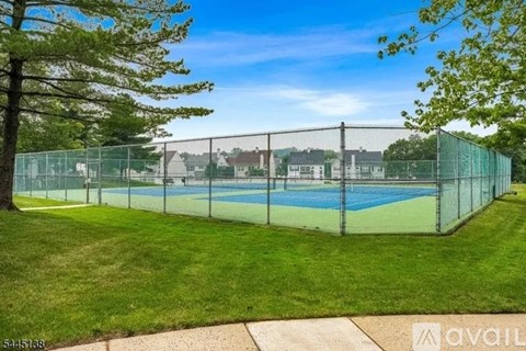 A tennis court surrounded by a green fence and trees.