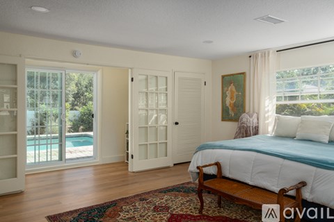 A bedroom with a large bed and a pool outside the window.