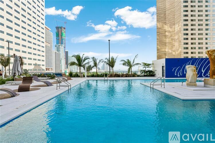 A large swimming pool surrounded by palm trees and lounge chairs with a cityscape in the background.