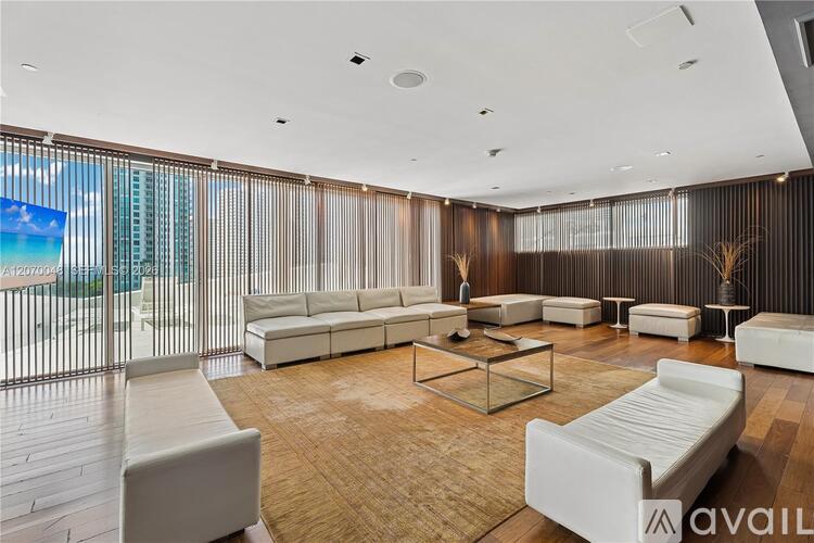 A spacious living room with white furniture and a large window overlooking the beach.