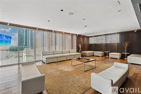 A spacious living room with white furniture and a large window overlooking the beach.