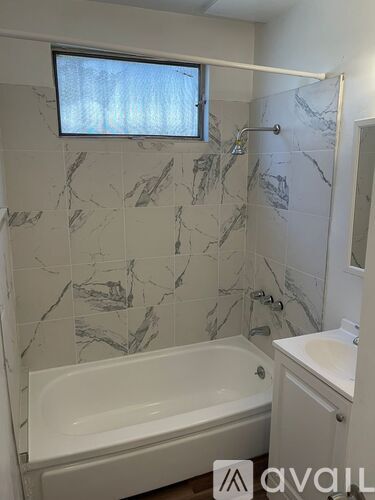 A bathroom with a marble tile wall and a white bathtub.