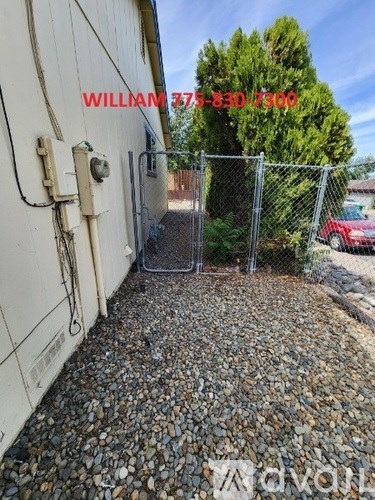 A gravel driveway leads to a white building with a red car parked behind a chain link fence.