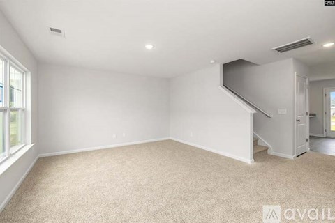 A room with a carpeted floor and a staircase on the right side.