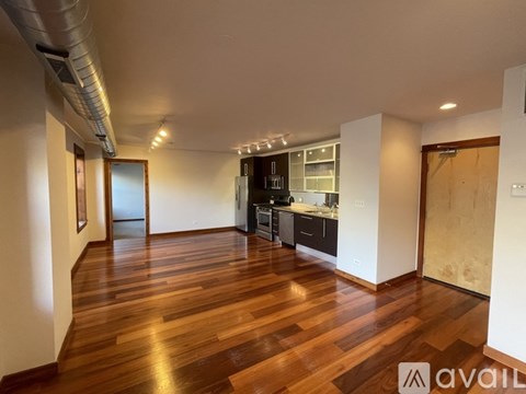 A spacious room with wooden flooring and a kitchen area in the background.