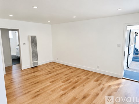 A spacious room with wooden flooring and a window with blinds.