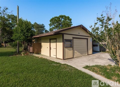 A two-car garage with a brown roof and tan walls is surrounded by green grass and trees.