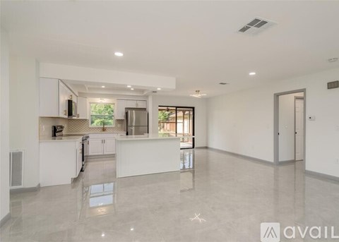 A spacious, empty living room with a kitchen area in the background.