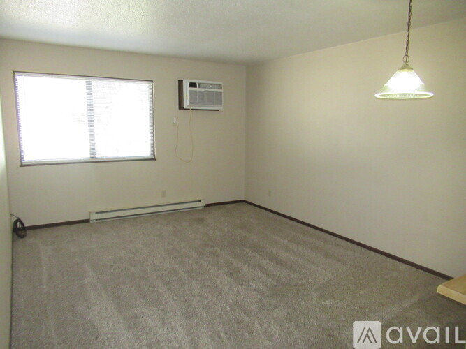 A room with a carpeted floor, a window, a ceiling fan, and a wall-mounted air conditioner unit.