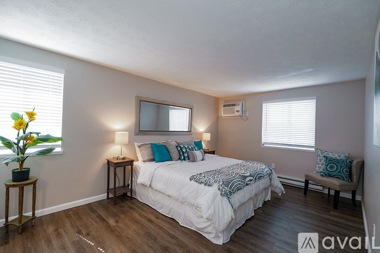 A bedroom with a bed, two lamps, a chair, and a vase of flowers.
