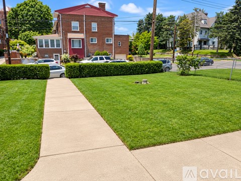 A red brick house with a white door and windows, a green lawn, and a sidewalk in front.