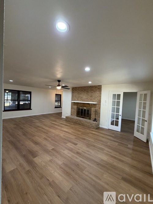 A spacious room with wooden flooring and a brick fireplace.