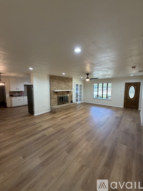 A spacious room with wooden flooring and a brick fireplace.