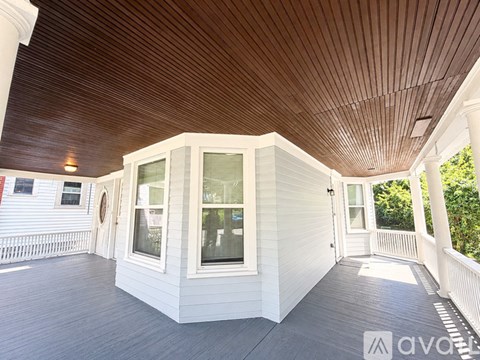 A wooden deck with a white house and a wooden ceiling.