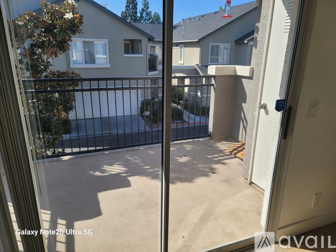 A view from a window looking out to a patio with a black railing and a tree.