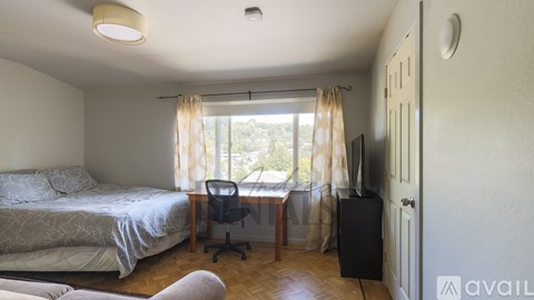 A bedroom with a bed, desk, chair, and a window with curtains.