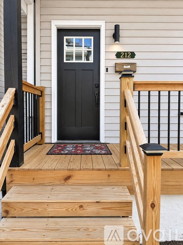 A black door with a glass window is flanked by a wooden railing.