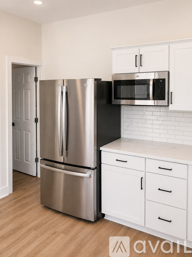 A kitchen with a stainless steel refrigerator and microwave, white cabinets, and a white subway tile backsplash.