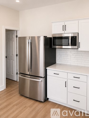 A kitchen with a stainless steel refrigerator and microwave, white cabinets, and a white subway tile backsplash.