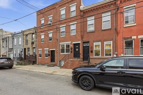 A black car is parked in front of a brick building with a sign that reads "available.".