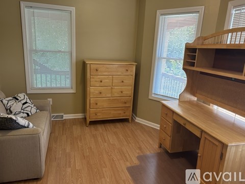 A room with a couch, a dresser, and a desk with a window.