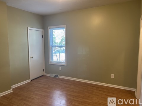 A room with a door, a window, and a wooden floor.