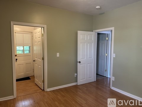 A room with two doors, one of which is open, and a window with a view of trees.